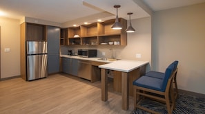 A modern kitchen with a stainless steel refrigerator, wooden cabinets, a microwave, and a sink.