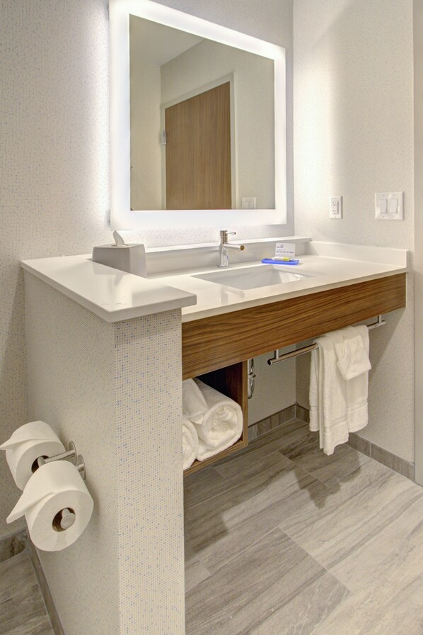 A modern bathroom with a large mirror, white sink, and wooden vanity.