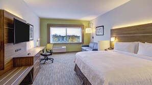Ein Hotelzimmer mit Bett, Schreibtisch, Stuhl, Fernseher und einem Fenster mit Blick auf Bäume.
