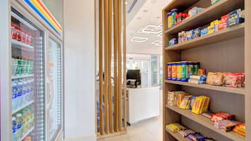 En butiksinredning med hyllor fyllda med olika produkter, ett kylskåp och en avskärmande väggpanel i trä.