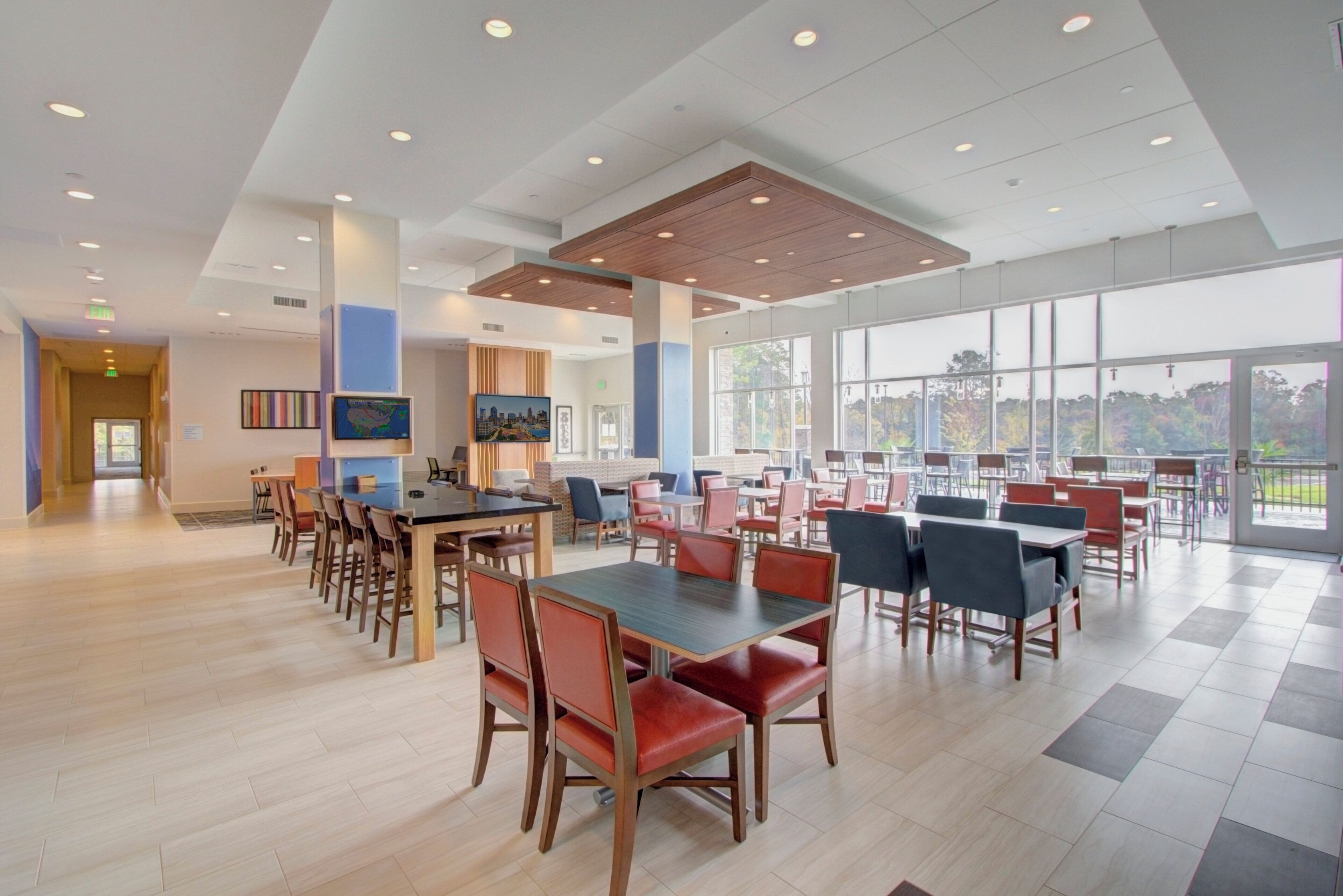A spacious indoor dining area with multiple tables and chairs, large windows offering a view, and a modern ceiling design.