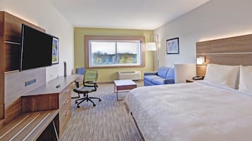 Una habitación de hotel con cama, escritorio con silla, televisor, ventana con vistas y lámpara.