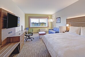 Una habitación de hotel con cama, escritorio con silla, televisor, ventana con vistas y lámpara.