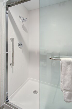 A glass-enclosed shower area with a white tiled wall, a glass door, and a white towel hanging on a towel bar.