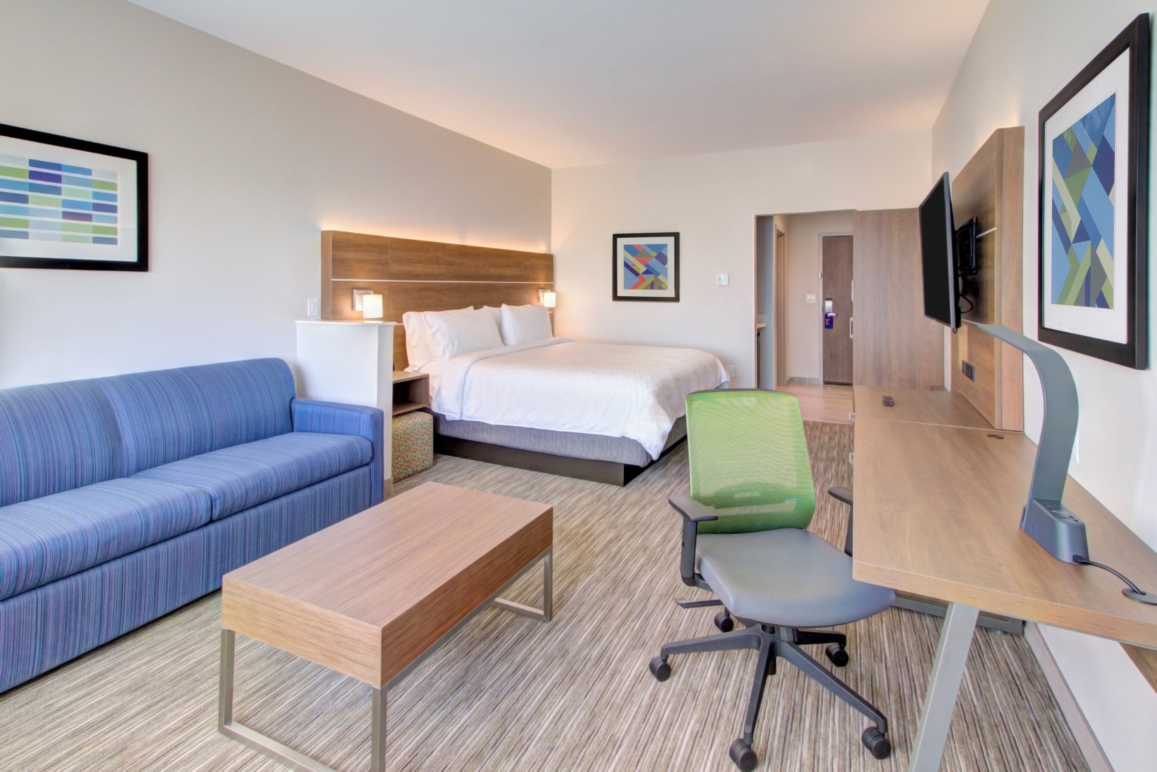 A hotel room with a bed, a blue sofa, a desk with a chair, and a television.