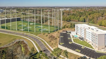 A multi-story hotel with a parking lot, a baseball field, and a road with a curve.