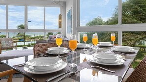 Un coin repas avec une table dressée pour quatre personnes, de grandes fenêtres et une vue sur l’océan.