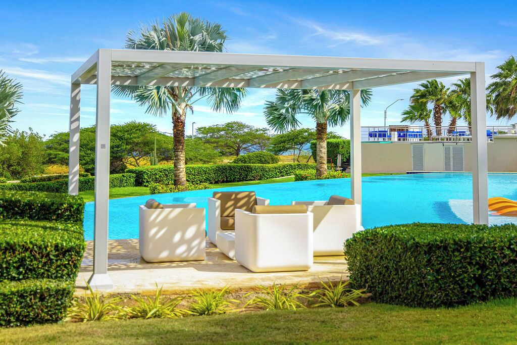 A poolside area with a covered seating area, palm trees, and a clear blue pool.