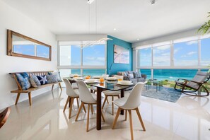 Enjoy a panoramic ocean view from this spacious living area with a dining table, sofa, and large window.