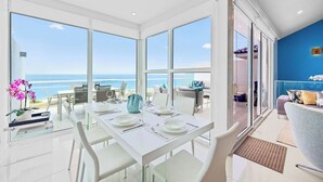 A dining area with a view of the ocean, white furniture, and a blue accent wall.