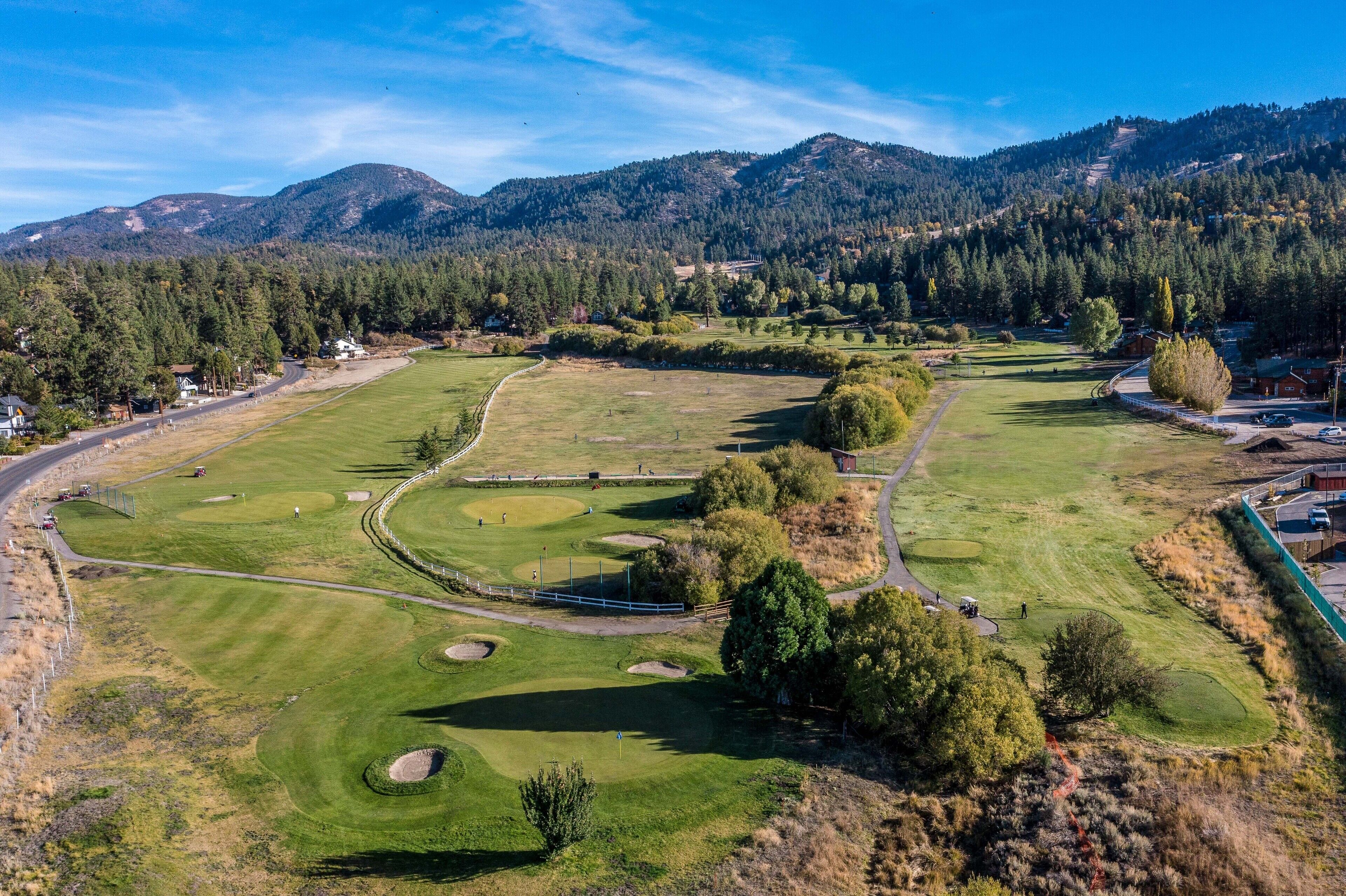 A golf course with a clear view of the surrounding landscape, including mountains and trees.