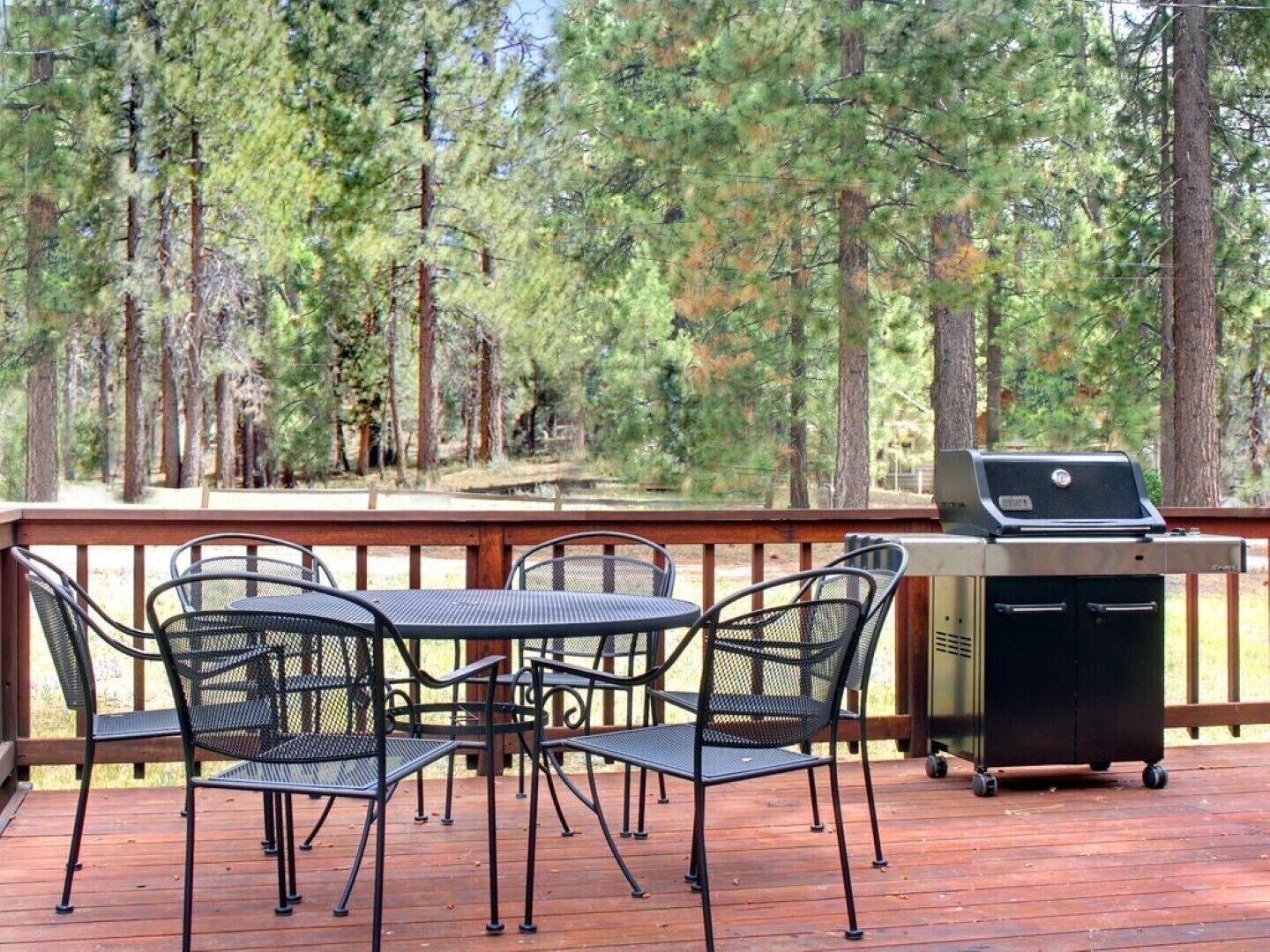 Una terraza exterior con una parrilla, sillas de metal y una mesa.