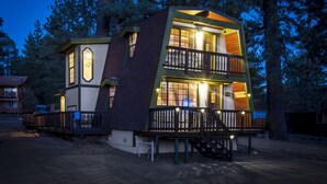 A two-story wooden cabin with a balcony, surrounded by trees.