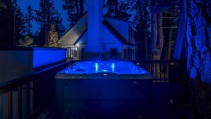 A hot tub in a backyard with a stone chimney, surrounded by trees.