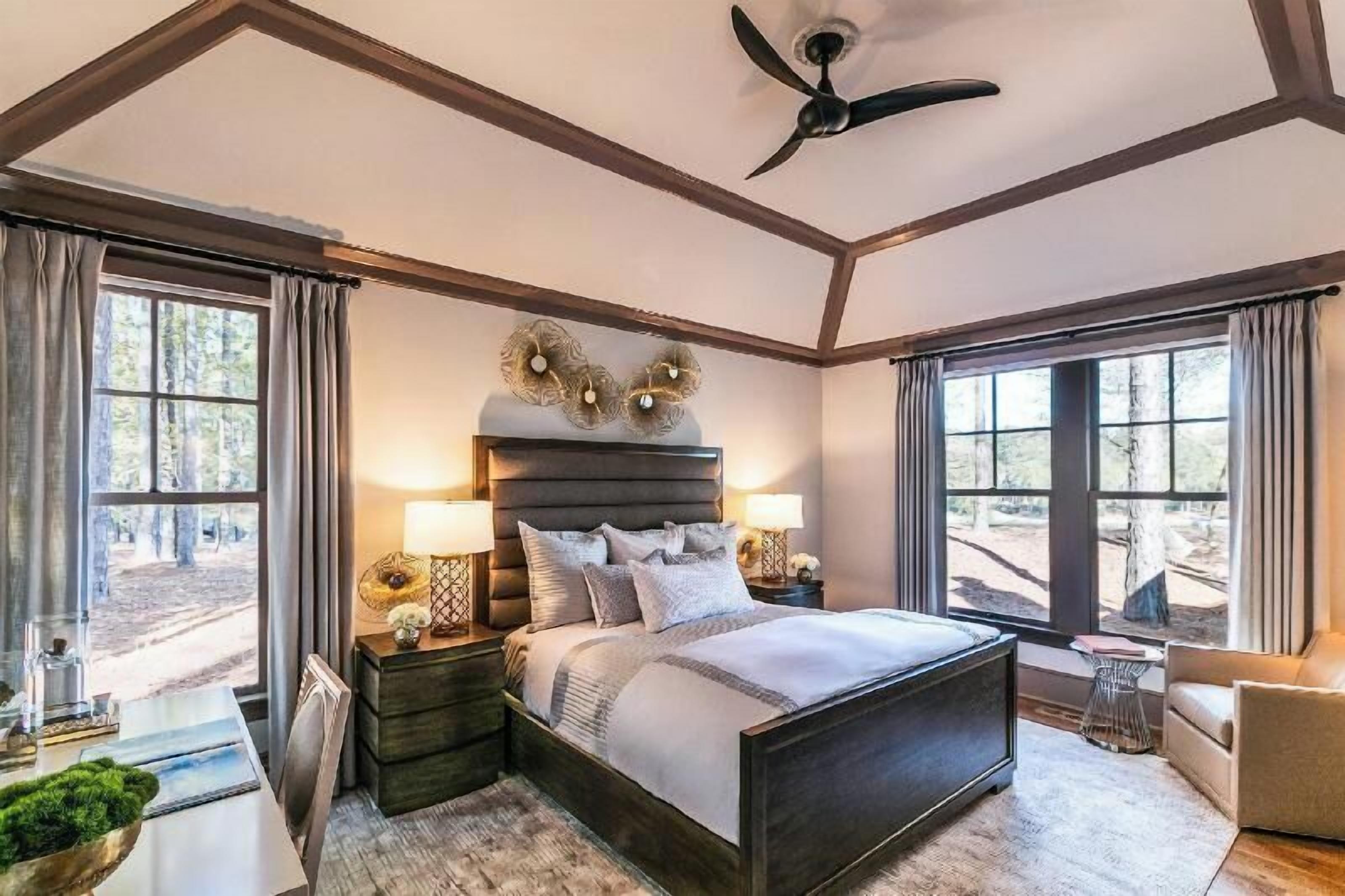 A bedroom with a large bed, two bedside tables, a ceiling fan, and a view of the outdoors.