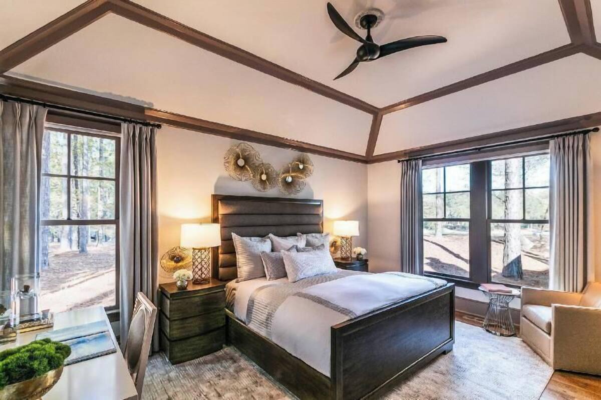 A bedroom with a large bed, two bedside tables, a ceiling fan, and a view of the outdoors.