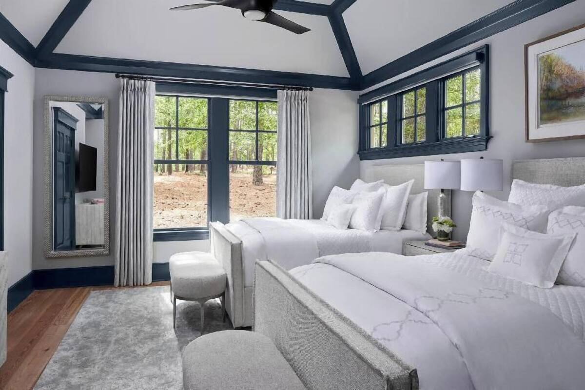 A bedroom with a large bed, two bedside tables, a ceiling fan, and a view of the outdoors.