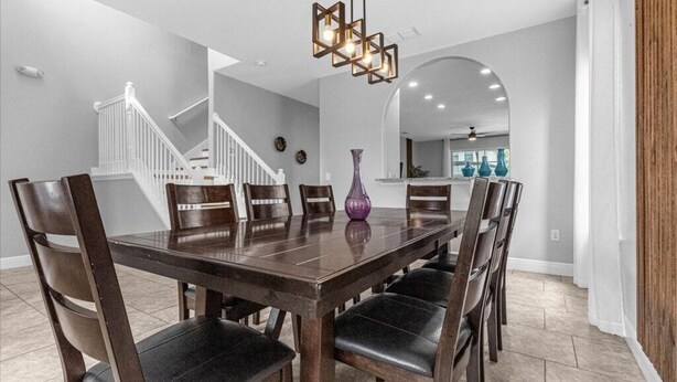 Une salle à manger avec une table et des chaises en bois, un vase violet et un escalier en arrière-plan.