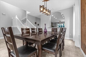 A dining room with a wooden table and chairs, a purple vase, and a staircase in the background. - 5 Bedrooms / 4 Bathrooms /  Solterra (5357 OA) (Davenport)