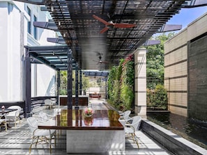 Un patio al aire libre con una mesa larga y sillas, un ventilador de techo y un jardín vertical.