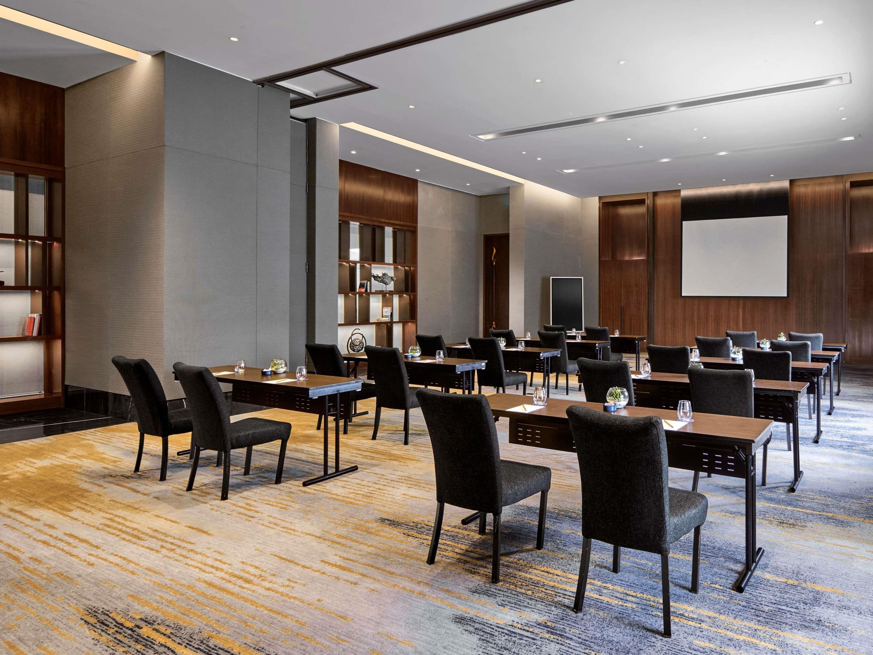 A conference room with multiple tables and chairs, a projector screen, and a bookshelf.