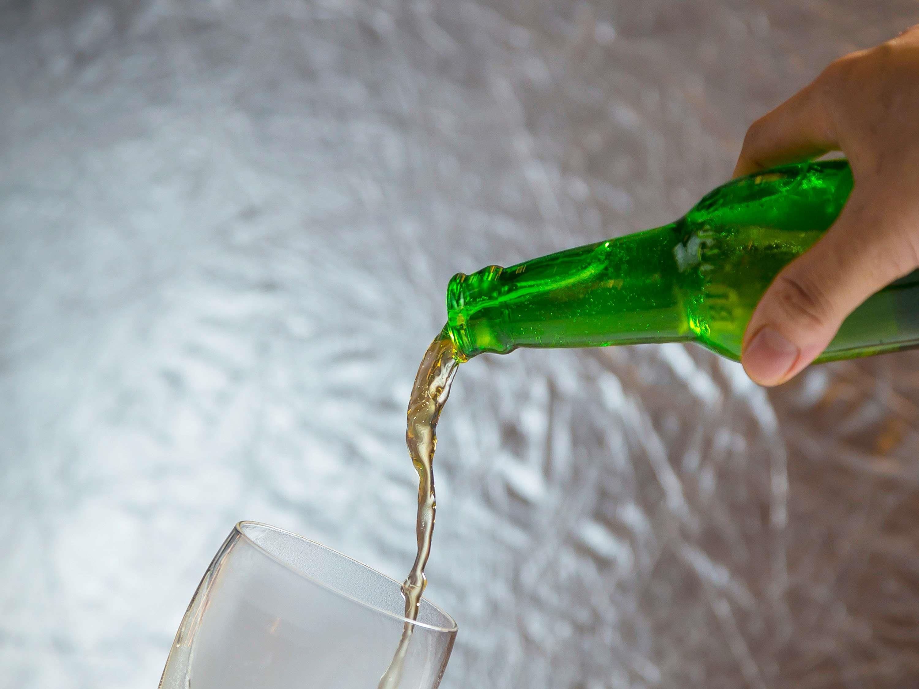 Een hand giet een vloeistof uit een groene fles in een helder glas.