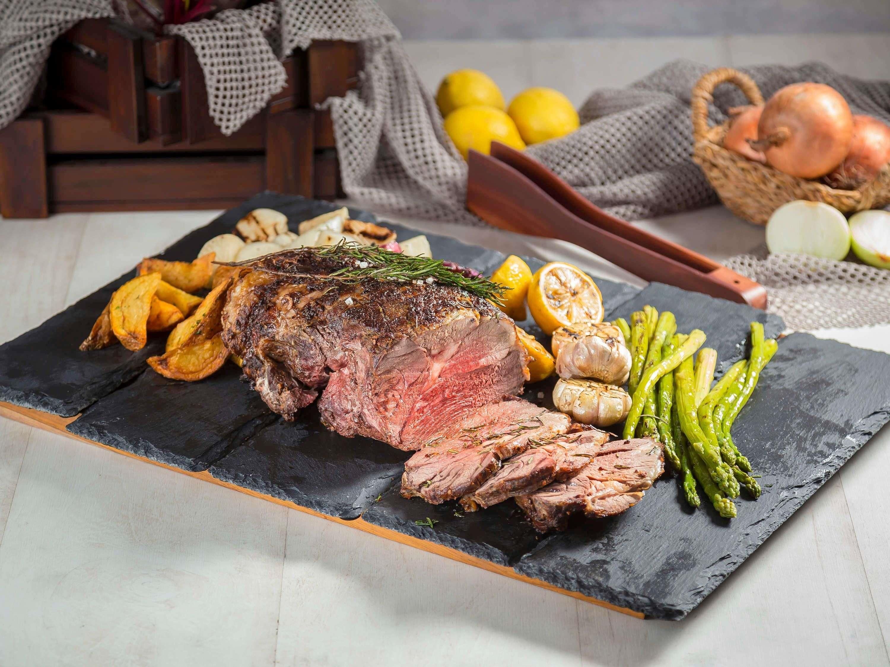 A roasted beef steak with vegetables on a slate board.