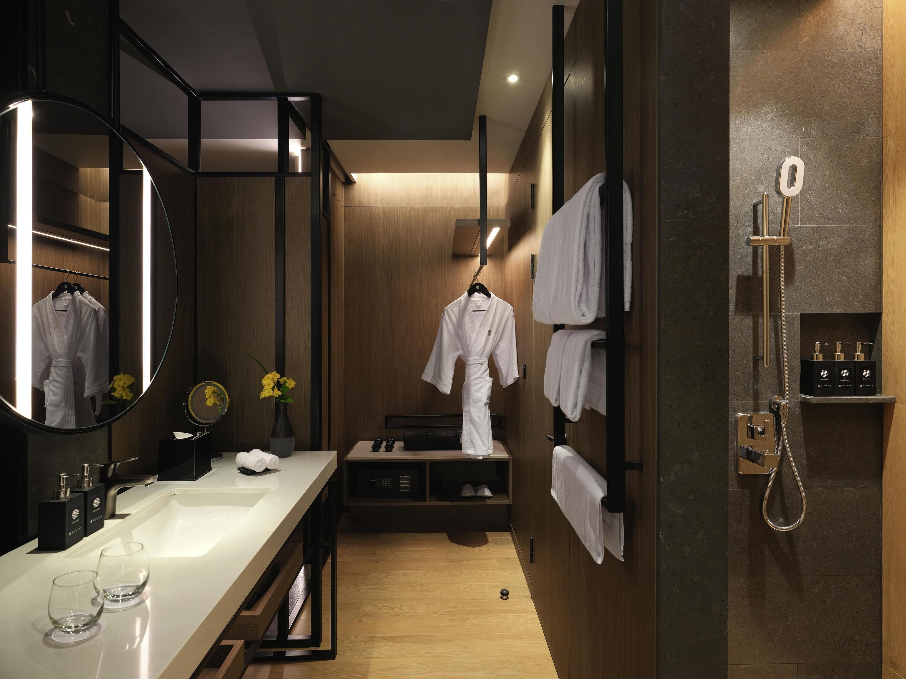 A modern bathroom with a wooden vanity, a large mirror, a shower with a handheld showerhead, and neatly arranged towels.