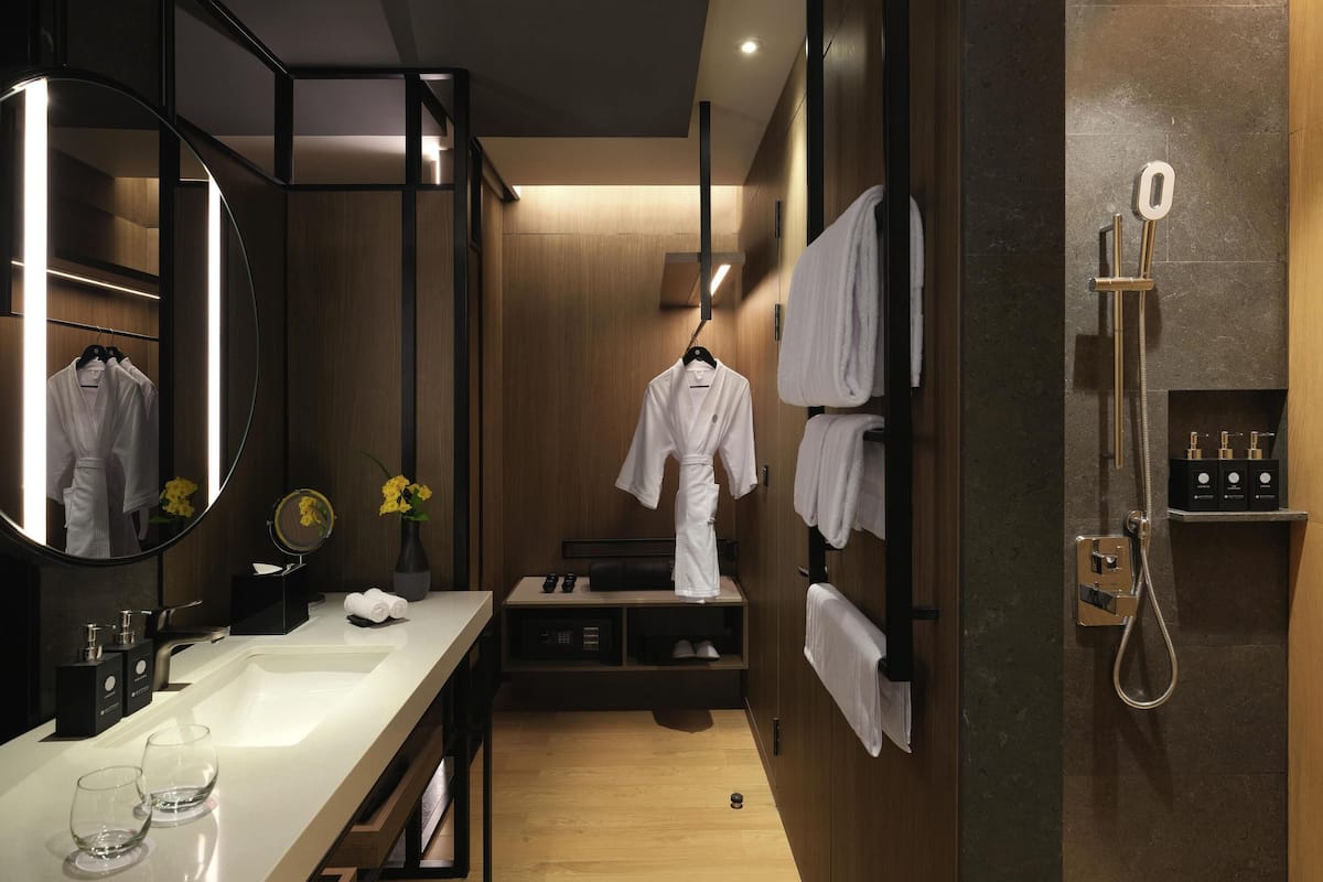Un baño moderno con tocador de madera, un espejo grande, ducha con cabezal de ducha manual y toallas ordenadas.
