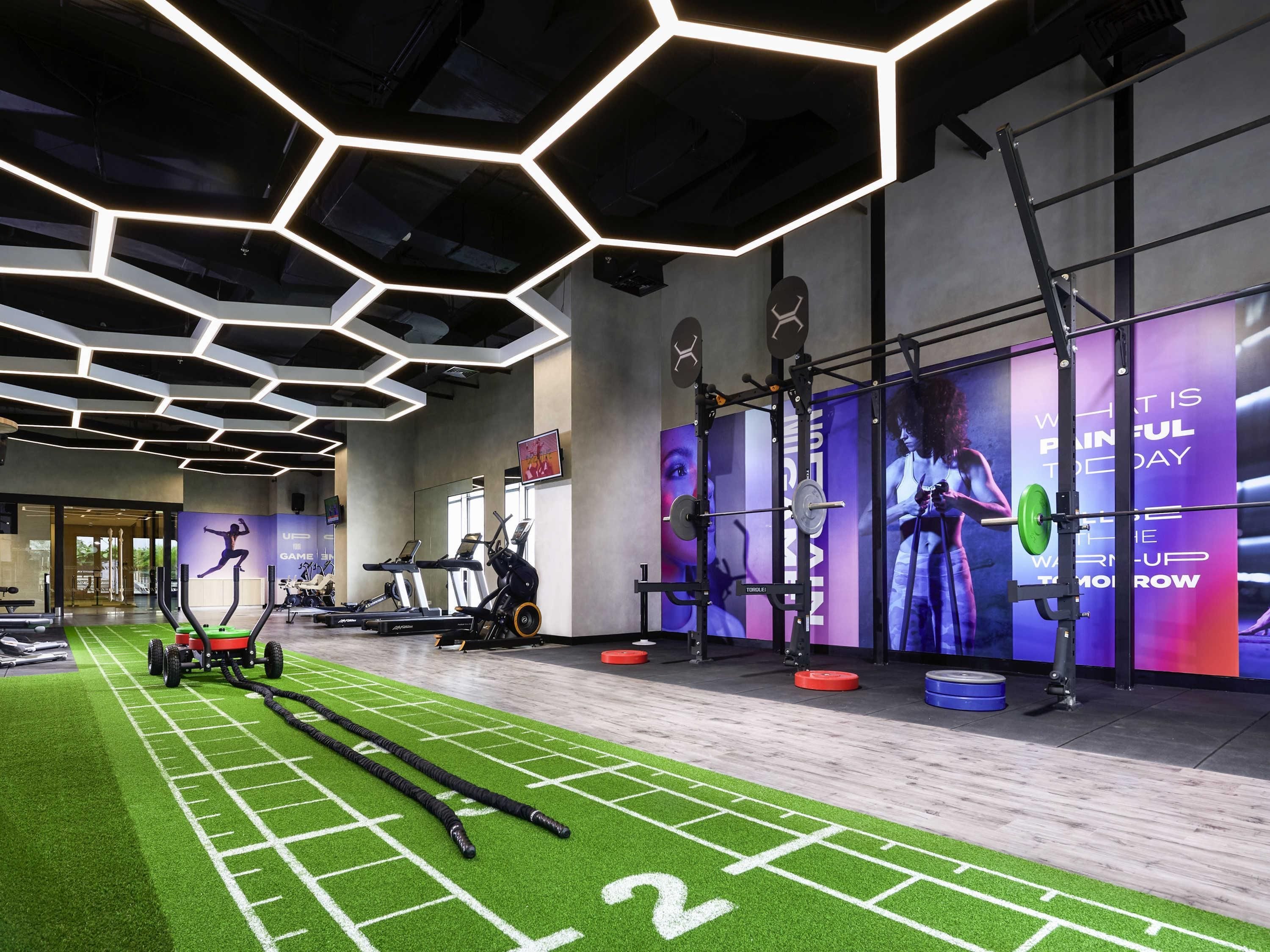 A gym with exercise equipment, a green turf area, and a hexagonal ceiling design.