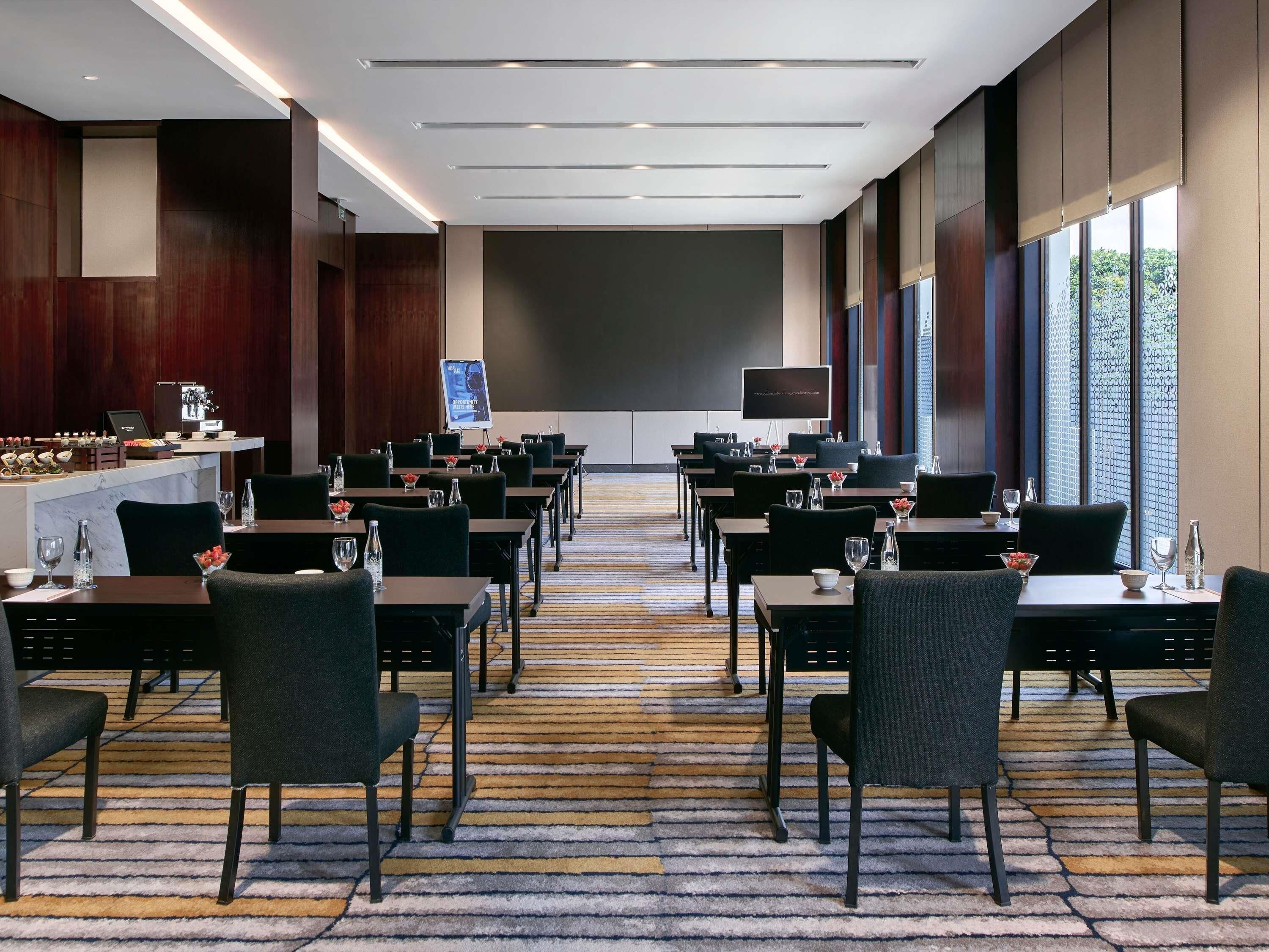 A conference room with tables, chairs, a projector screen, and a presentation board.