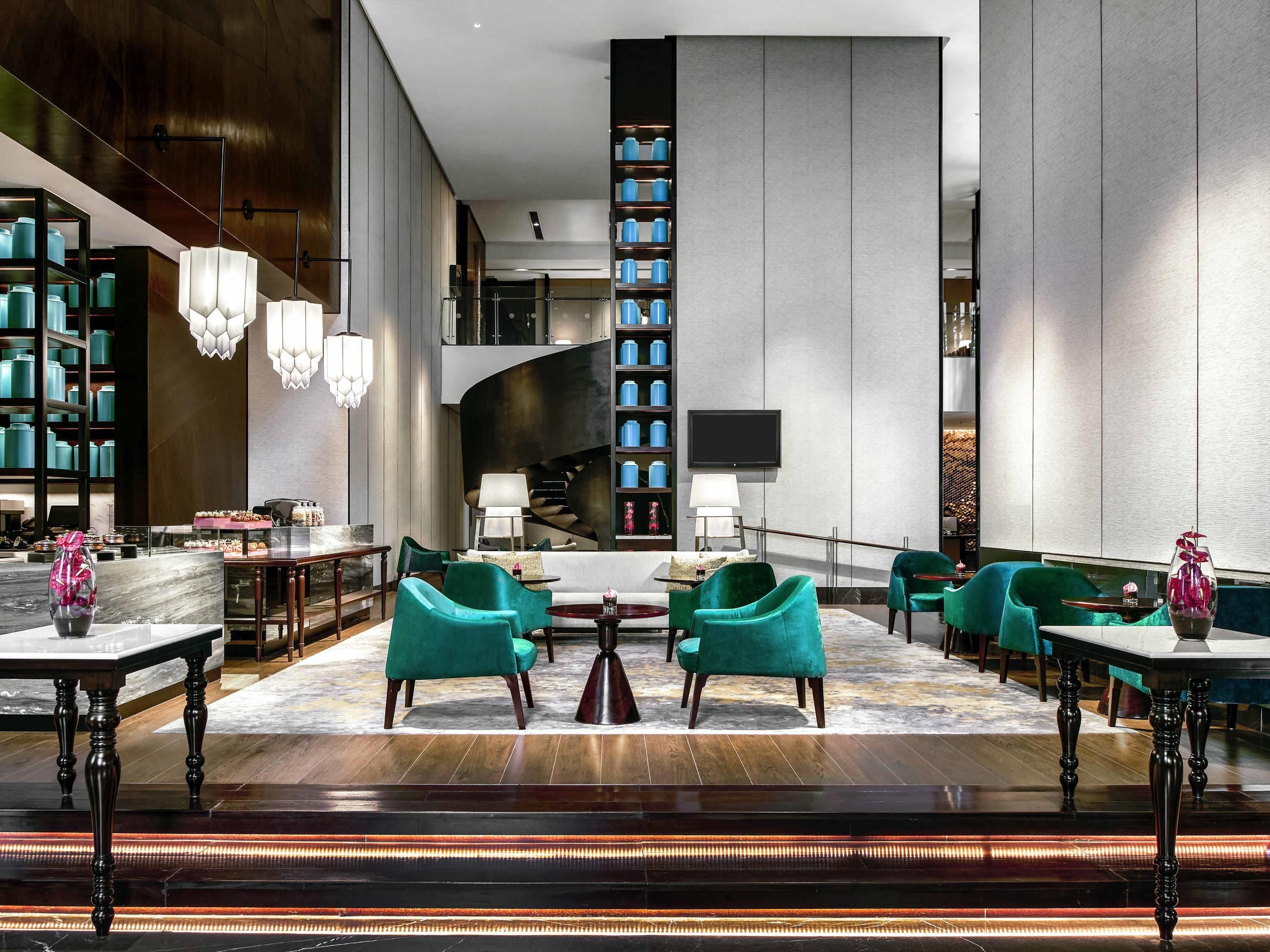 A modern lobby with teal chairs, a fireplace, a TV, and a bookshelf.