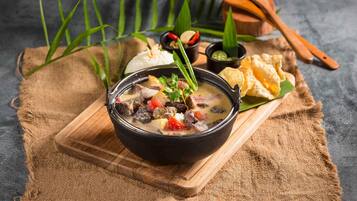 A bowl of stew with vegetables and meat, accompanied by a side of bread and dipping sauces on a wooden board.