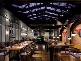 Un restaurante con largas mesas de madera, sillas y un diseño moderno en el techo.