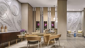 A modern dining area with a central round table, two chairs, and a decorative wall with peacock feather patterns.
