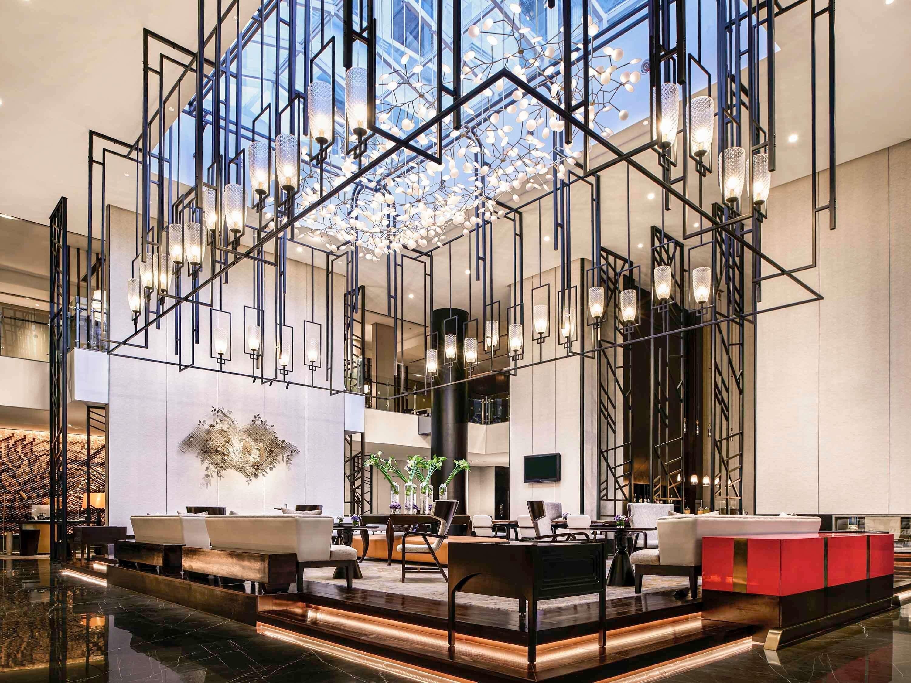 Un hall d’entrée moderne agrémenté d’un lustre aux motifs géométriques, de coins salon et d’un grand élément décoratif mural.
