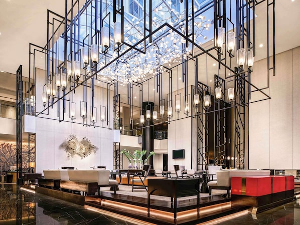 A modern lobby with a geometric chandelier, seating areas, and a large decorative wall piece.