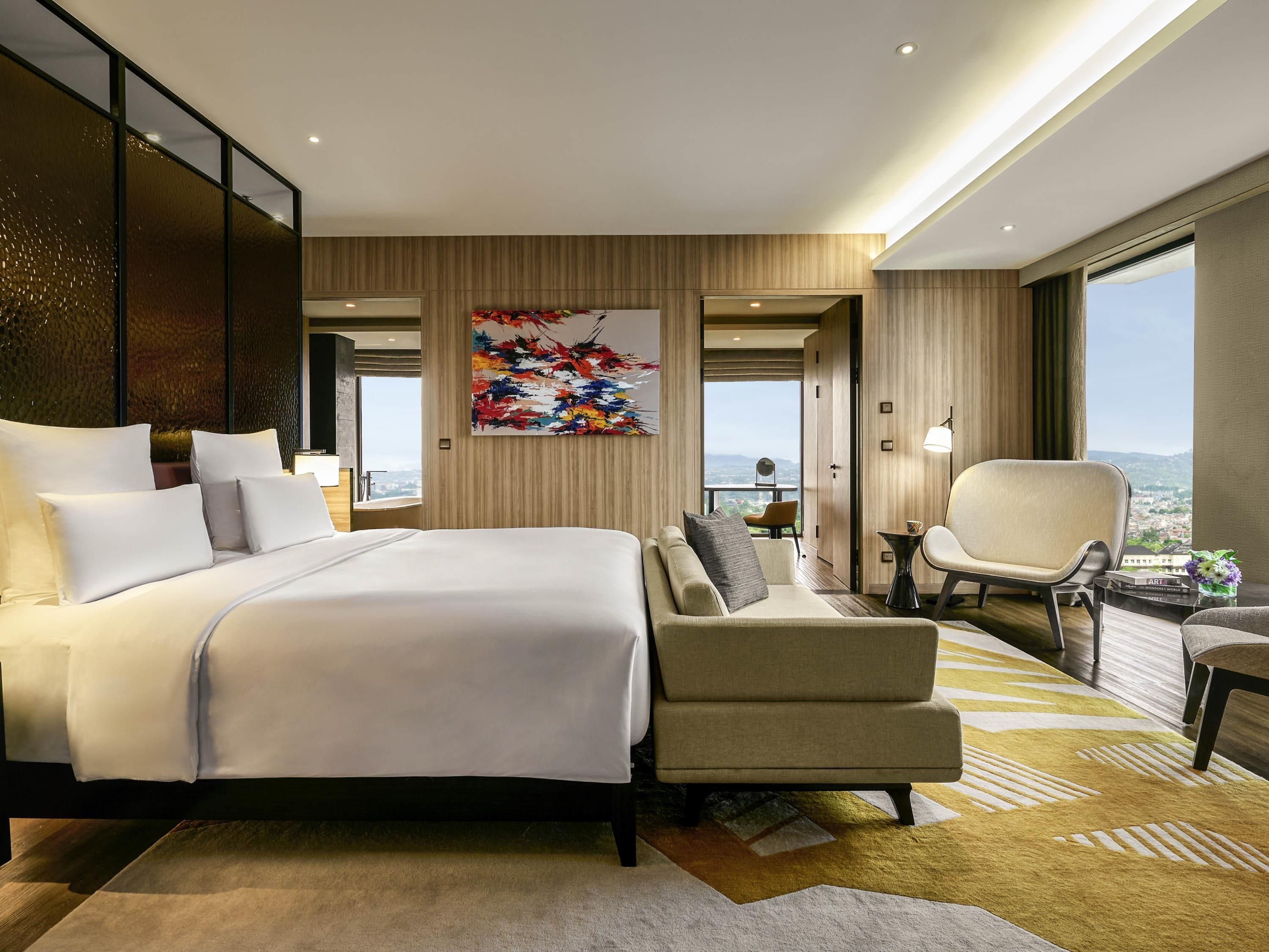 Una habitación de hotel moderna con una cama grande, un sofá, una silla y vistas a la ciudad.