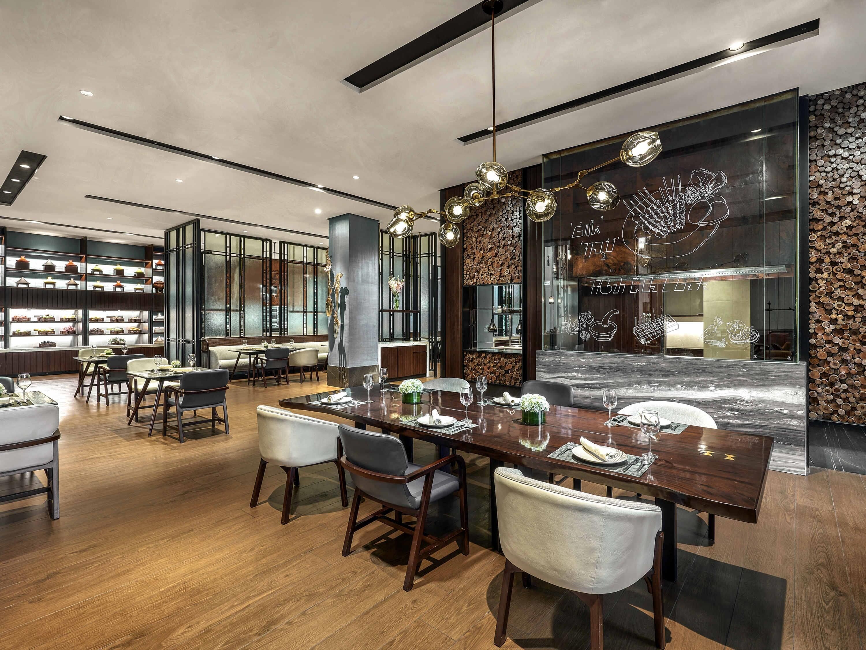 A modern dining area with a long wooden table, chairs, and a decorative wall with a fireplace.