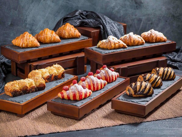 A variety of pastries displayed on wooden stands against a dark background. - Pullman Bandung Grand Central (Bandung)