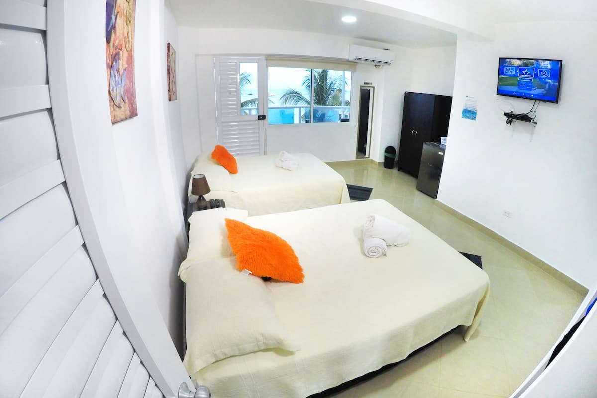 Habitación de hotel con dos camas, un televisor montado en la pared y vistas al exterior a través de la ventana.