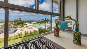 Une chambre dotée d’une grande fenêtre donnant sur une piscine et un jardin, un lit avec un oreiller bleu et un vase avec une plante.