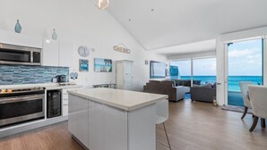 Een moderne keuken met een centraal eiland, een eetgedeelte met uitzicht op de oceaan en een woonkamer met een groot raam dat uitkijkt over de zee.
