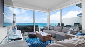 Een moderne woonkamer met een groot raam met uitzicht op de oceaan, een bank, een salontafel en een klein bureau met decoratieve objecten.