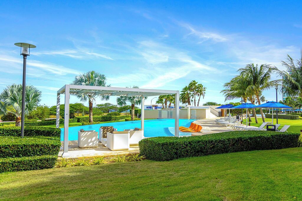 Ein Poolbereich mit Liegestühlen, einer  überdachten Sitzgelegenheit und blauem Himmel.