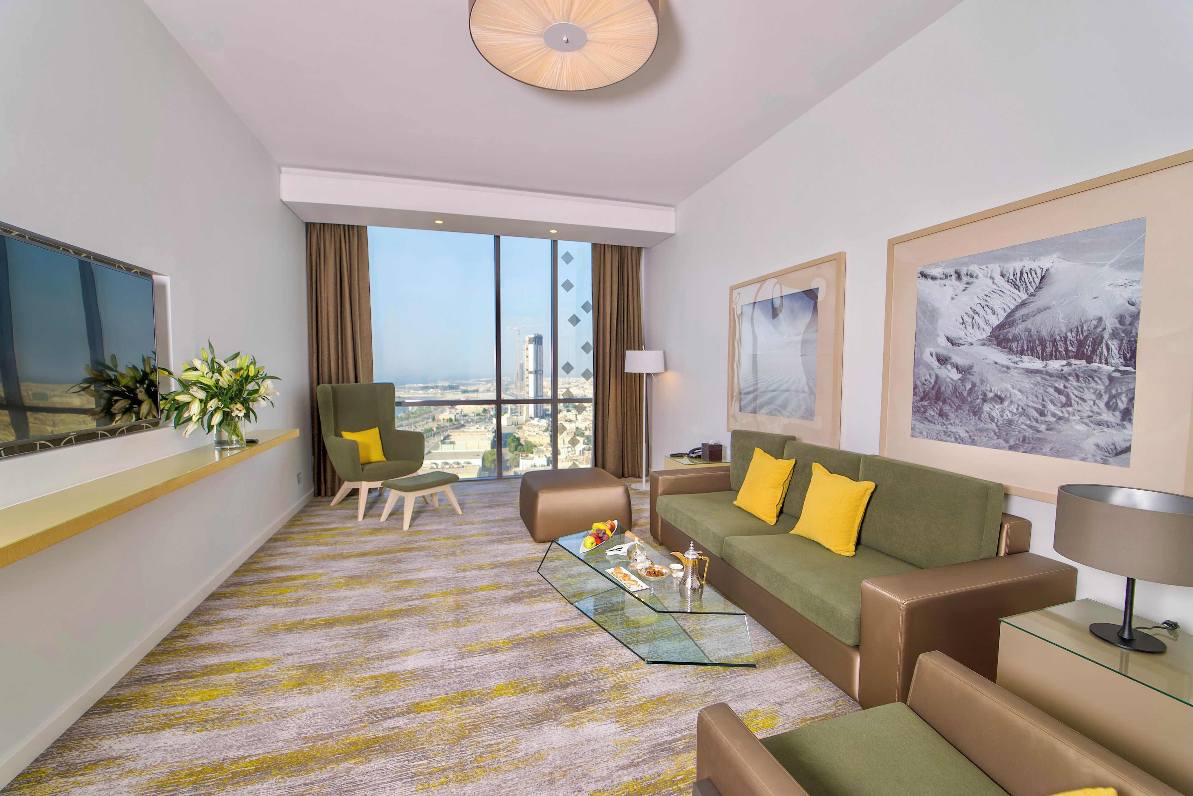 Une chambre d’hôtel moderne dotée d’une grande fenêtre, d’un canapé, d’un fauteuil, d’une table basse et d’un téléviseur.
