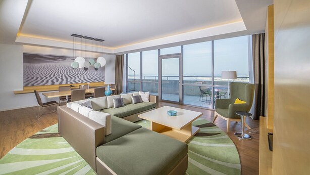 Habitación de hotel moderna con un amplio sofá, una zona de comedor y un balcón con vistas al océano.