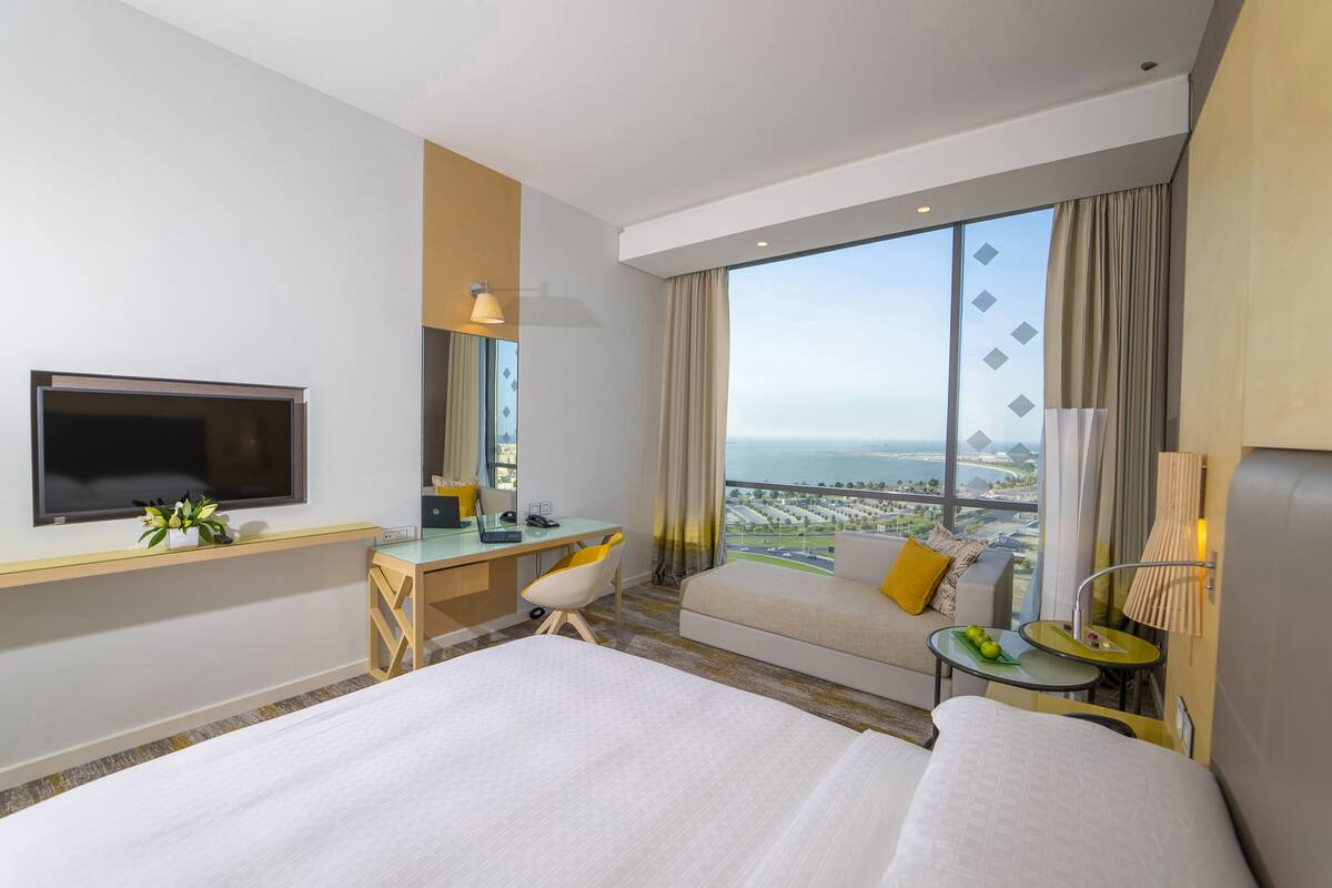 A hotel room with a bed, a desk, a TV, a sofa, and a view of the city.