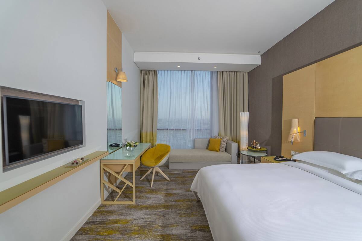 A hotel room with a bed, a desk, a chair, a TV, and a window with curtains.