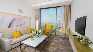 Habitación de hotel moderna con sofá, sillón, mesa de centro y un gran ventanal con vistas a la ciudad.